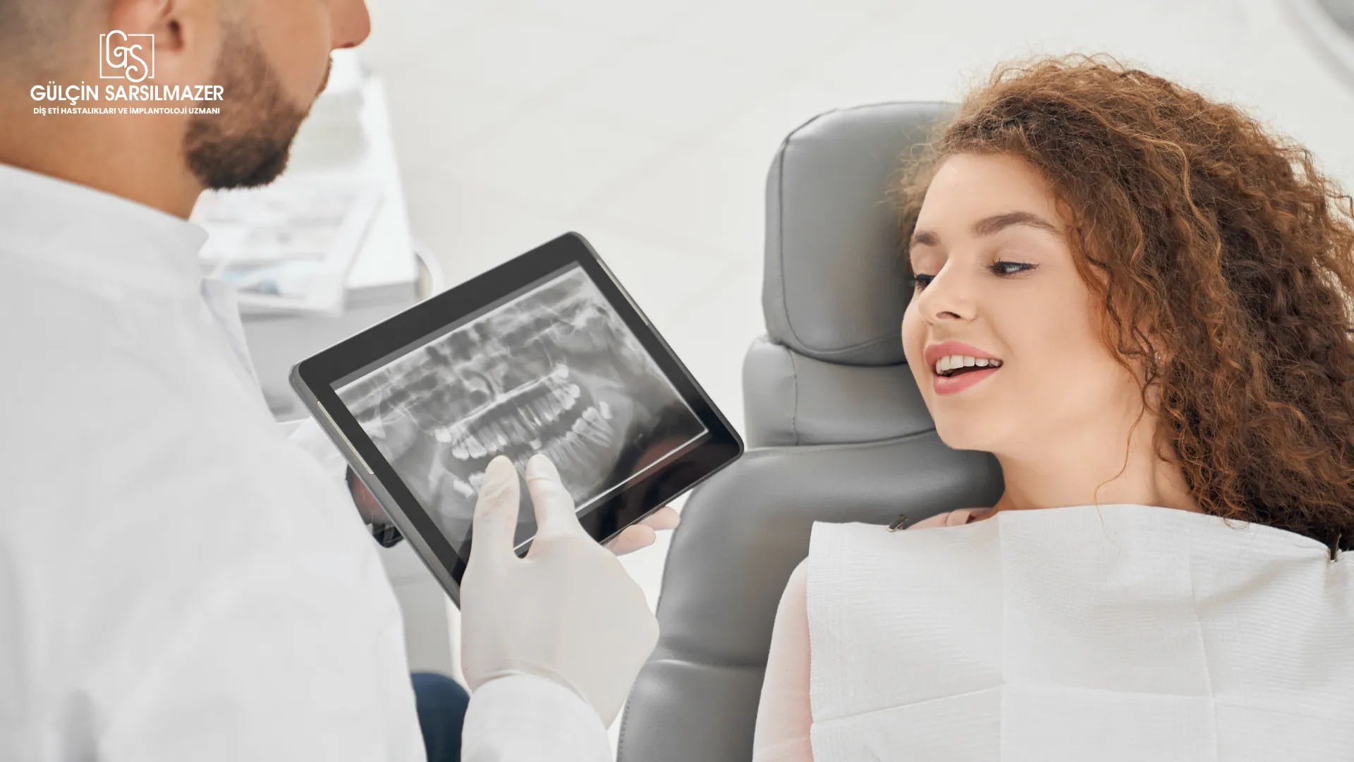 Diş hekimi, hastaya tablette implant planlaması için panoramik röntgen gösteriyor.